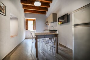 A kitchen with a wooden ceiling, a built-in oven, a refrigerator, and a window with wooden shutters.