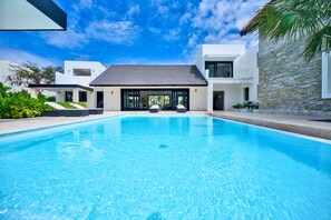 A modern pool area with clear blue water, surrounded by white buildings and greenery. - Cayuco 6-Luxury Ocean Villa on Hole #5 of Punta Espada w/Staff Close to St Regis (Cap cana)