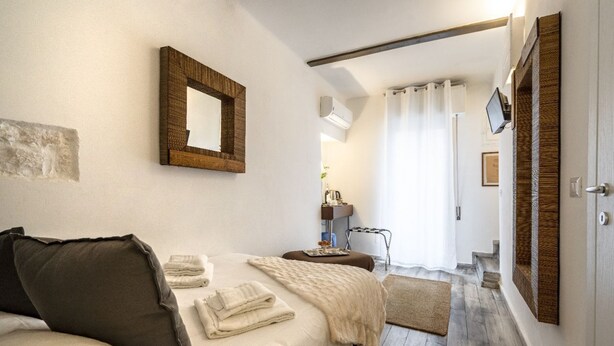 Une chambre à coucher avec un lit, un miroir, une télévision, et une salle de bain visible au fond.