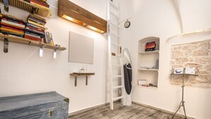 Une pièce avec un plancher en bois, une commode bleue, une échelle, une étagère remplie de livres et une horloge au mur.