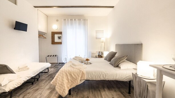 Een hotelkamer met twee bedden, een bureau, een stoel, een televisie, een spiegel, een raam met gordijnen en een nachtkastje.
