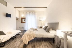 Habitación de hotel con dos camas, un escritorio, una silla, un televisor, un espejo, una ventana con cortinas y una mesita de noche.