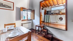 En matplats med ett bord för fyra personer, ett fönster med persienner, ett element och utsikt över ett kök med tvättmaskin.