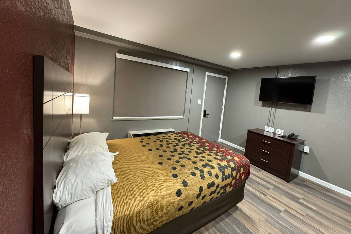 A hotel room with a bed, a TV mounted on the wall, a dresser, and a door.