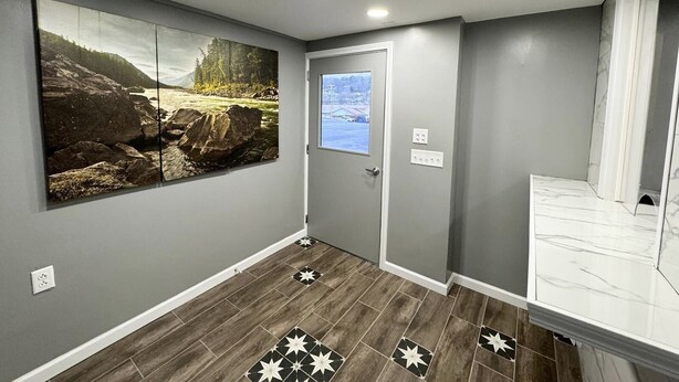 A hallway with grey walls, a large landscape painting, a door with a window, and a tiled floor with a geometric pattern. - Residency Inn & Studios (Waynesburg)