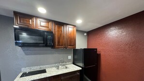 A kitchen with wooden cabinets, a black microwave, a black refrigerator, and a granite countertop. - Residency Inn & Studios (Waynesburg)