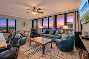 A modern living room with a large window, a ceiling fan, and a view of the city skyline at dusk.