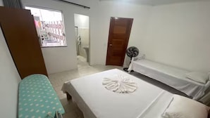 A bedroom with two beds, a fan, and an ironing board.