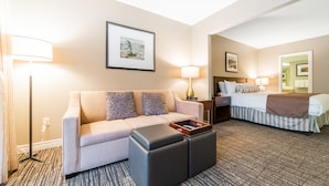 Une chambre d’hôtel comprenant un canapé, un pouf, une table de chevet, une lampe et un lit avec une couvre-lit à rayures.