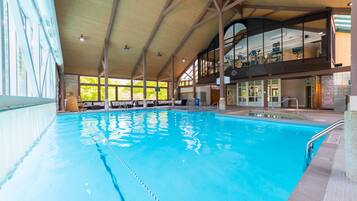 Piscina interior com pistas demarcadas, teto alto e vista para o andar superior com equipamentos de ginástica.