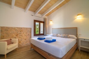 Un dormitorio con pared de piedra, una cama con toallas azules, cabecero de madera y una mesita de noche.