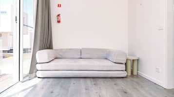 Uma sala de estar moderna com um sofá cinzento, uma mesa redonda pequena e um extintor de incêndio fixado na parede.