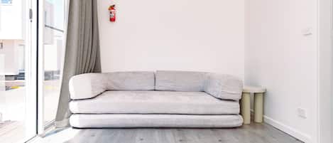 A modern living room with a grey sofa, a small round table, and a fire extinguisher mounted on the wall.