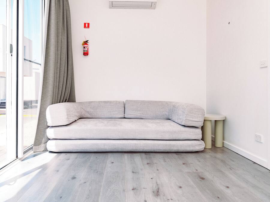 Uma sala de estar moderna com um sofá cinzento, uma mesa redonda pequena e um extintor de incêndio fixado na parede.