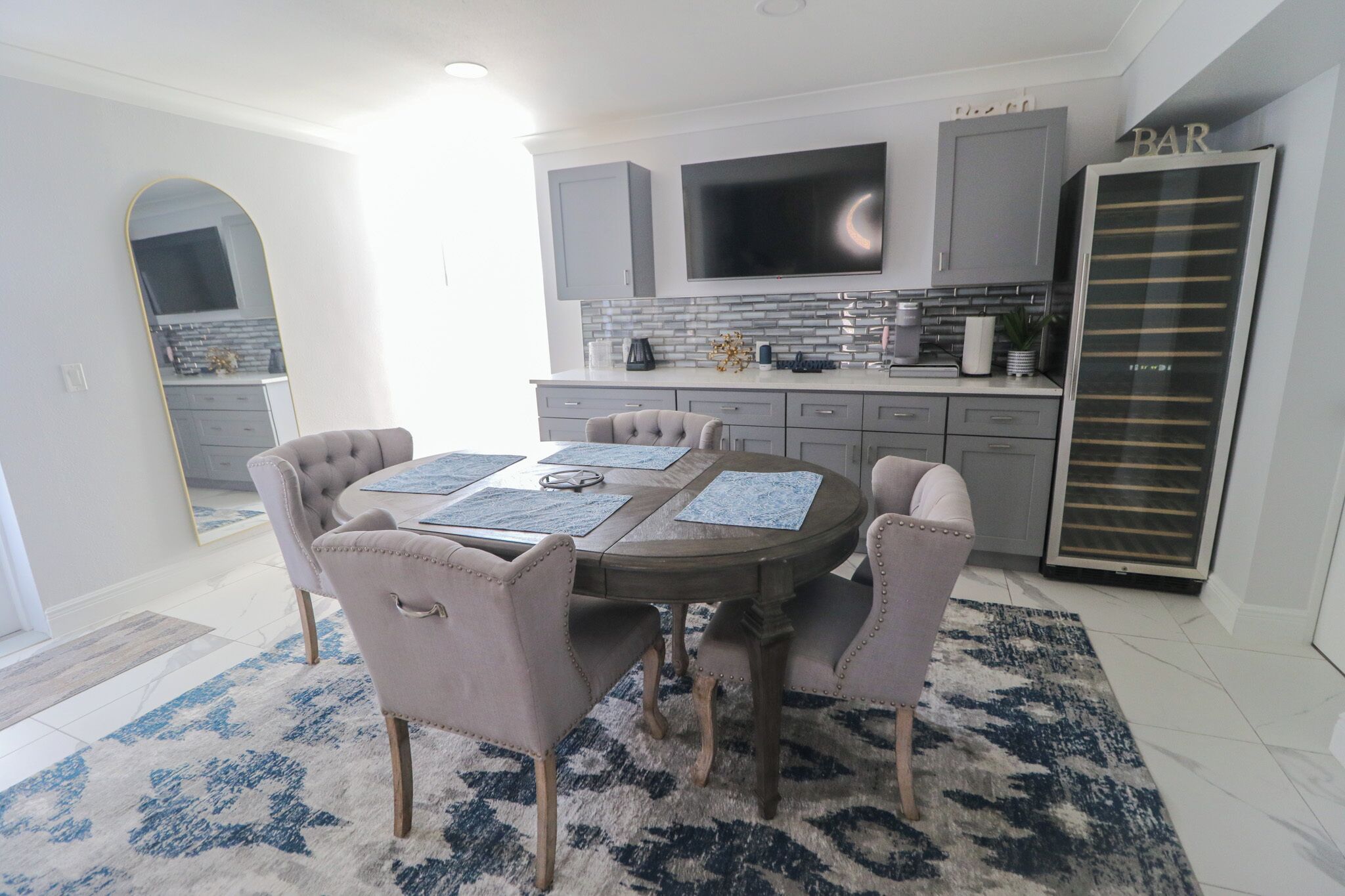 A modern kitchen with grey cabinets, a flat-screen TV, and a refrigerator with a 'BAR' sign.