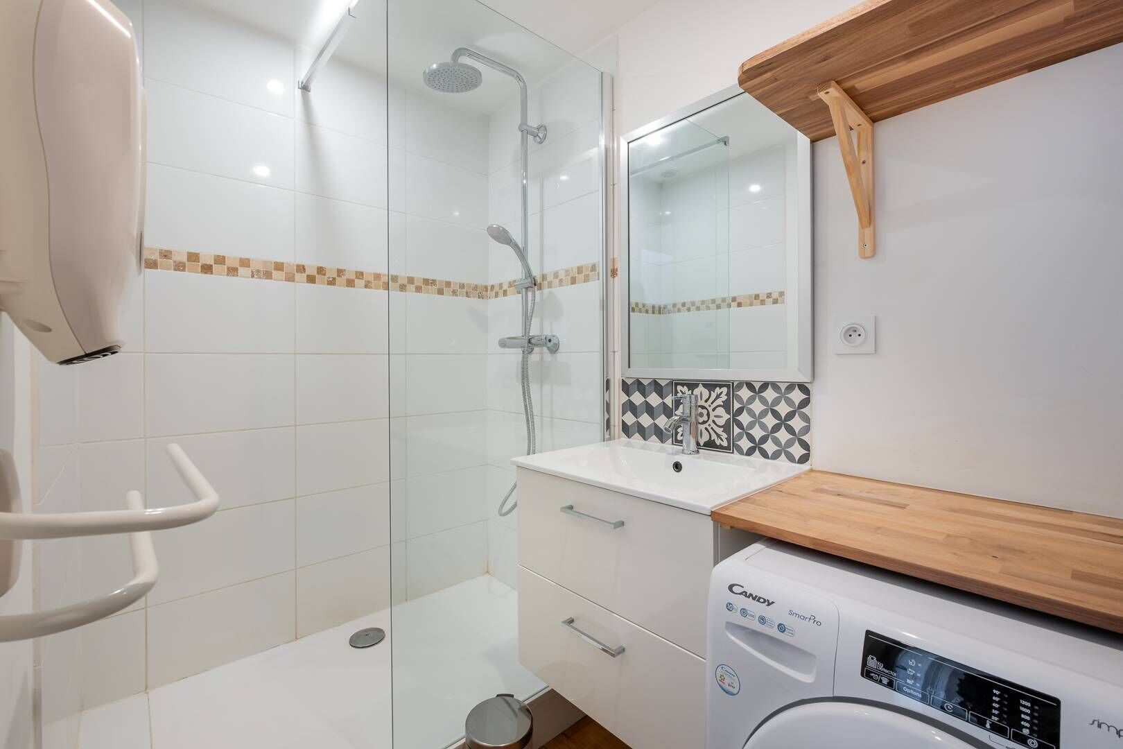 A modern bathroom with a glass shower enclosure, a built-in sink with a wooden countertop, and a wall-mounted washing machine.