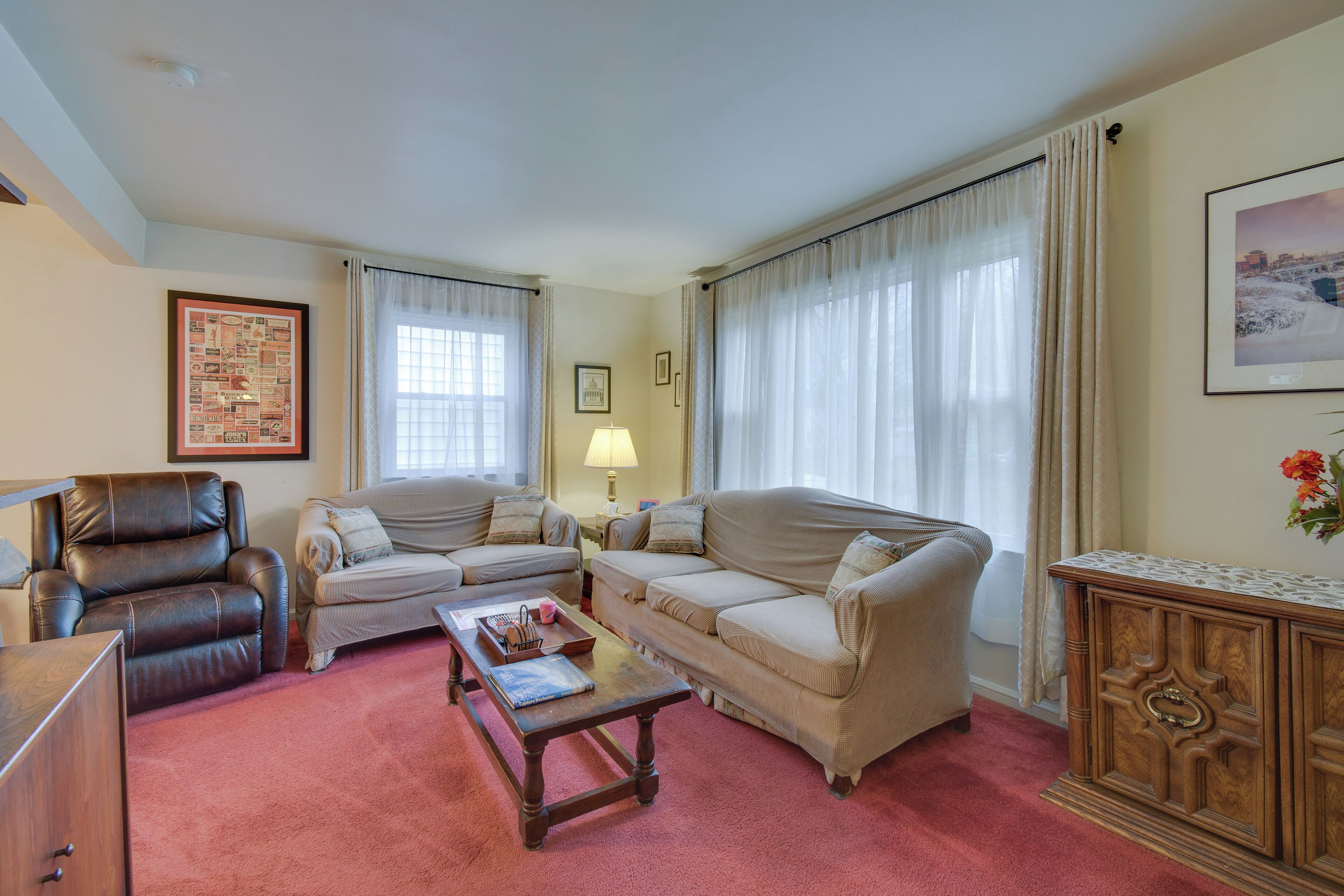 A living room with a brown leather armchair, beige sofas, a wooden coffee table, and a wooden cabinet.