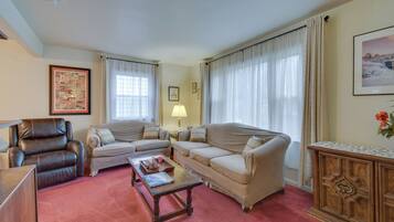 A living room with a brown leather armchair, beige sofas, a wooden coffee table, and a wooden cabinet.