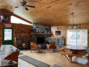 Interior acogedor de una cabaña con chimenea de piedra, muebles de madera y una puerta verde que indica 'EXIT'.