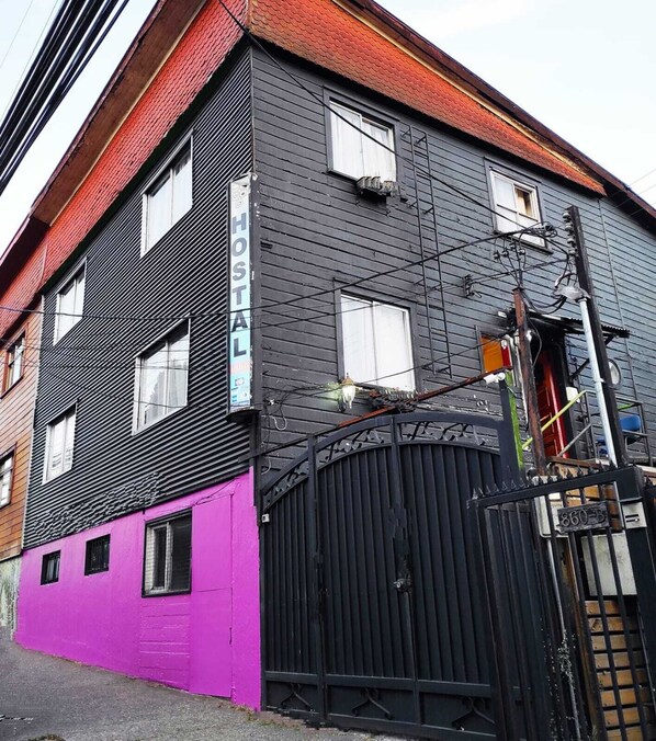 A building with a black exterior and a purple lower section, featuring a sign that reads "HOSTAL" and a black gate with a number "860-B".