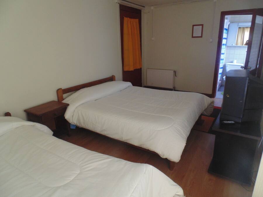 A room with two single beds, a wooden nightstand, a desk with a chair, a radiator, and a television.