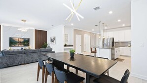 Una cocina moderna con armarios blancos, un refrigerador de acero inoxidable y un comedor con mesa y sillas de madera oscura.