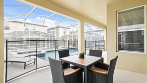 A covered outdoor area with a pool, wicker furniture, and a view of neighboring buildings. - Luxe Home w/ PS5, Pool, & Themed Rooms Near Disney (Orlando)