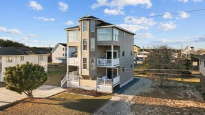A multi-story residential building with a balcony on the second floor, a covered front porch, and a driveway.
