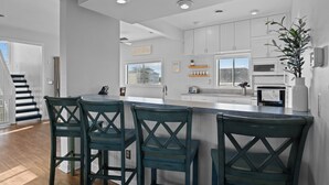 A modern kitchen with white cabinets, a central island with bar stools, and a staircase leading to another level.