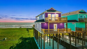 A two-story house with a balcony, wooden deck, and a view of the ocean. - Beachfront | Spacious, Pet-Friendly & Relaxing (Gilchrist)