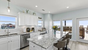A modern kitchen with white cabinets, a marble countertop, and a large island with bar stools. - Beachfront | Spacious, Pet-Friendly & Relaxing (Gilchrist)