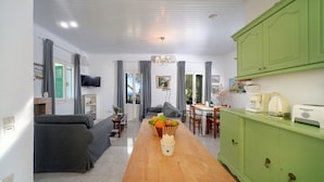 Una sala moderna con un sofá, una mesa de comedor con sillas, un mueble verde y un televisor.