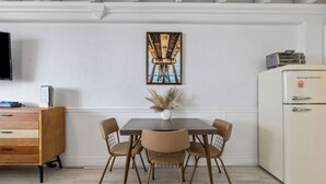 A dining area with a wooden table, four chairs, a vase with pampas grass, a vintage refrigerator, and a painting on the wall.