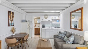 A modern kitchen with white cabinets, a dining area with a wooden table and chairs, and a gray sofa with patterned cushions.