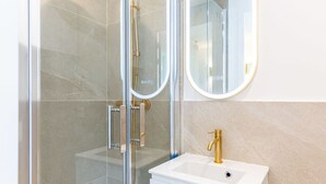A modern bathroom with a glass-enclosed shower, a white sink with a gold faucet, and a round mirror on the wall. - Lavie Maison: Equipped Studio, Chartrons (Bordeaux)