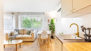 Een moderne woonkamer met een bank, eettafel en stoelen. Er is een keuken met een spoelbak en kastjes.