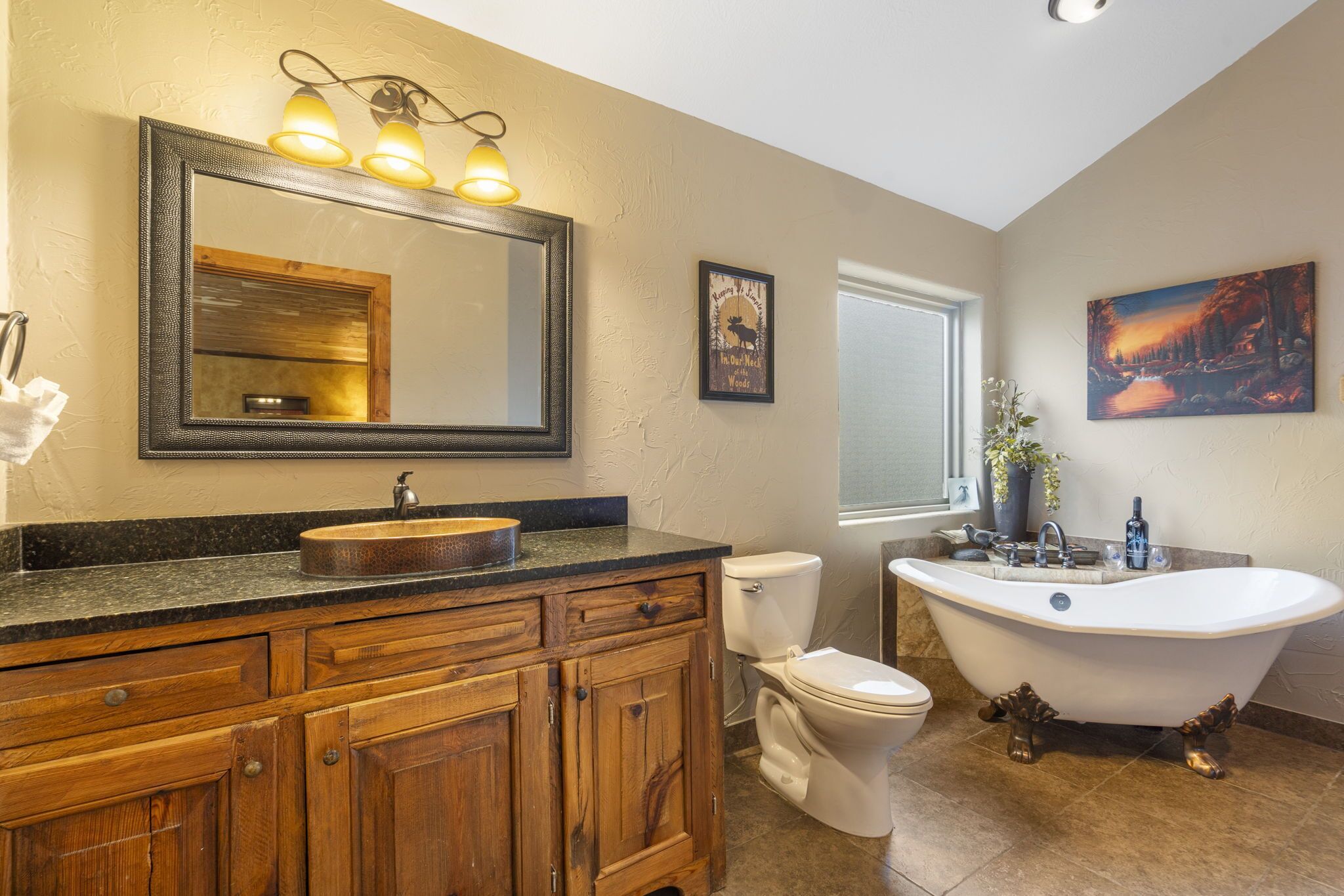 Une salle de bain avec une baignoire sur pieds, un meuble-lavabo en bois avec un évier, des toilettes et un grand miroir avec des appliques murales.