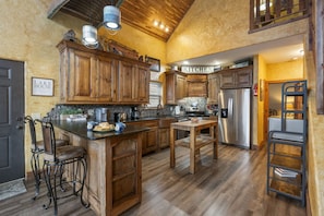 A spacious kitchen with wooden cabinets, a stainless steel refrigerator, and a bar area with stools. - Relaxing Lake Retreat w/ Views, Access, Private Hot Tub, Billiards & SDC Tickets (Branson)