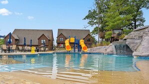 Une piscine avec un toboggan, des chaises longues et une cascade décorative.