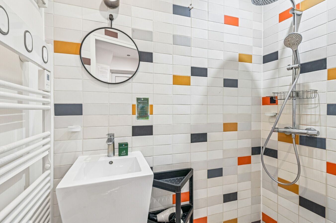 Ein Badezimmer mit einem weißen Waschbecken, einem Spiegel, einer Dusche inklusive Handbrause und einem Handtuchhalter.