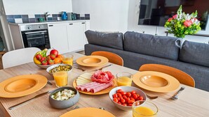 A dining table set with plates, cutlery, and various food items, with a kitchen and living area in the background.