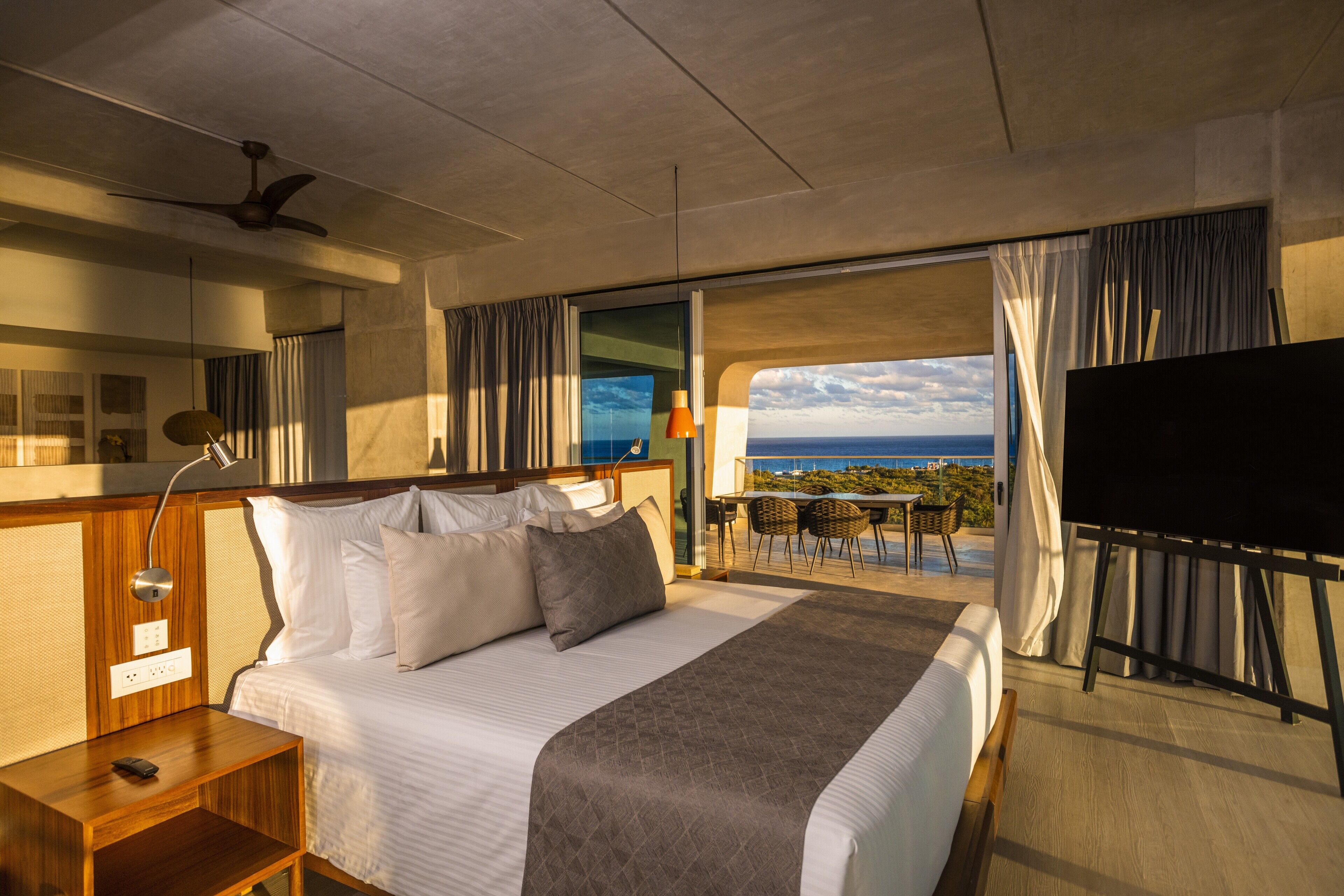 A hotel room with a bed, a desk, a TV, and a balcony with a view.