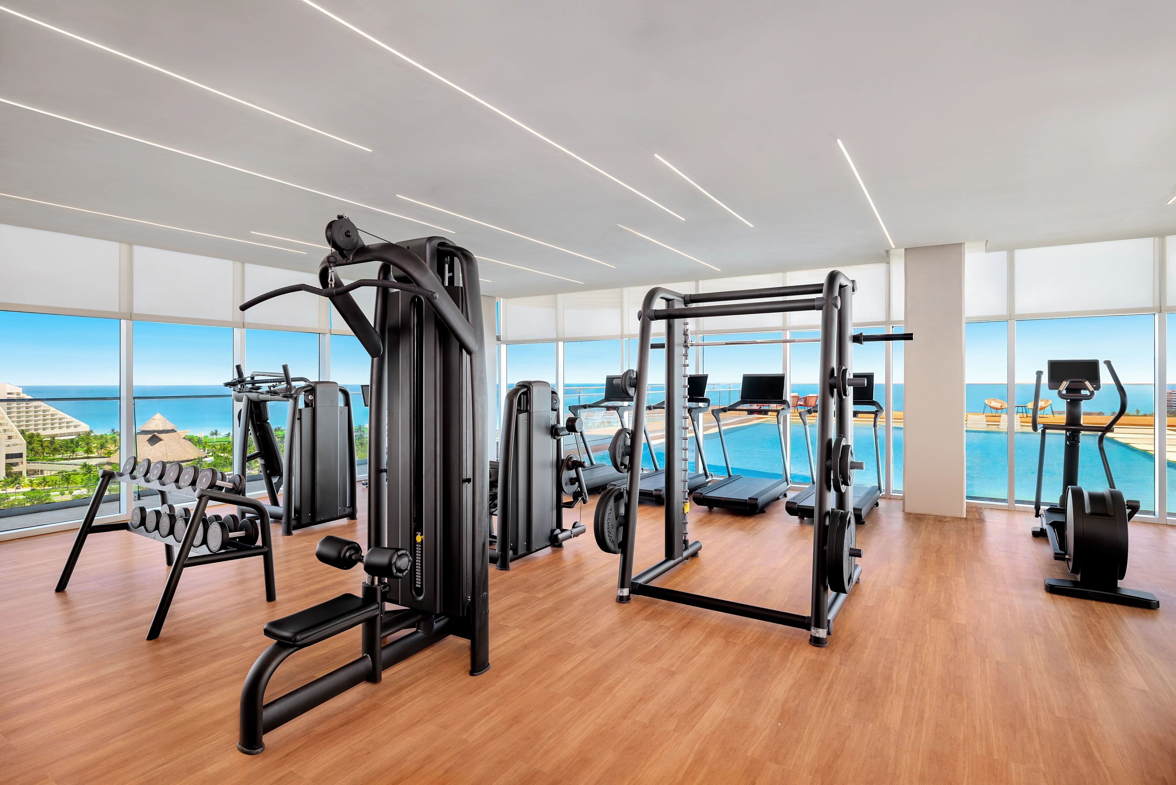 Een moderne sportschool met diverse fitnessapparaten, grote ramen en uitzicht op de oceaan.