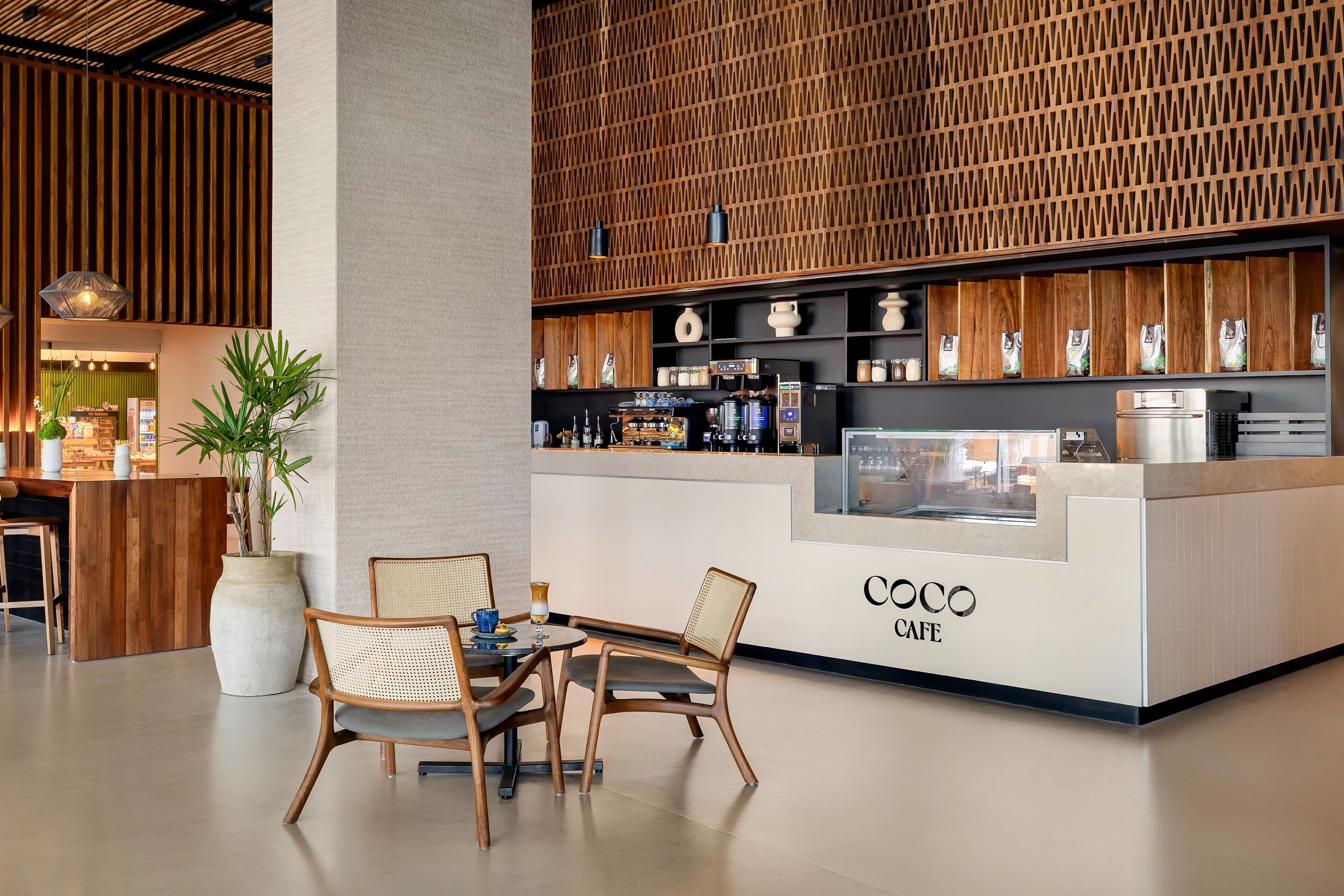 A modern cafe with a wooden interior, a counter with a coffee machine, and seating area with chairs and a table.