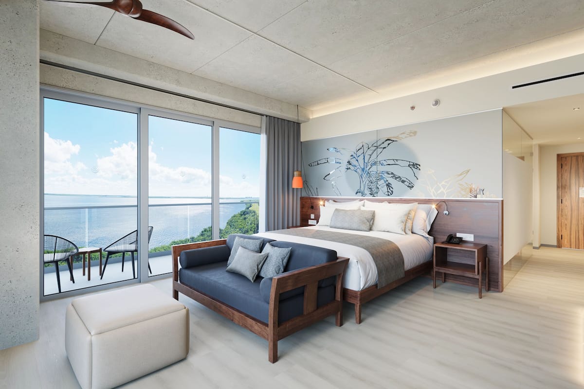 A modern bedroom with a large bed, a sofa, and a balcony with a view of the sea.