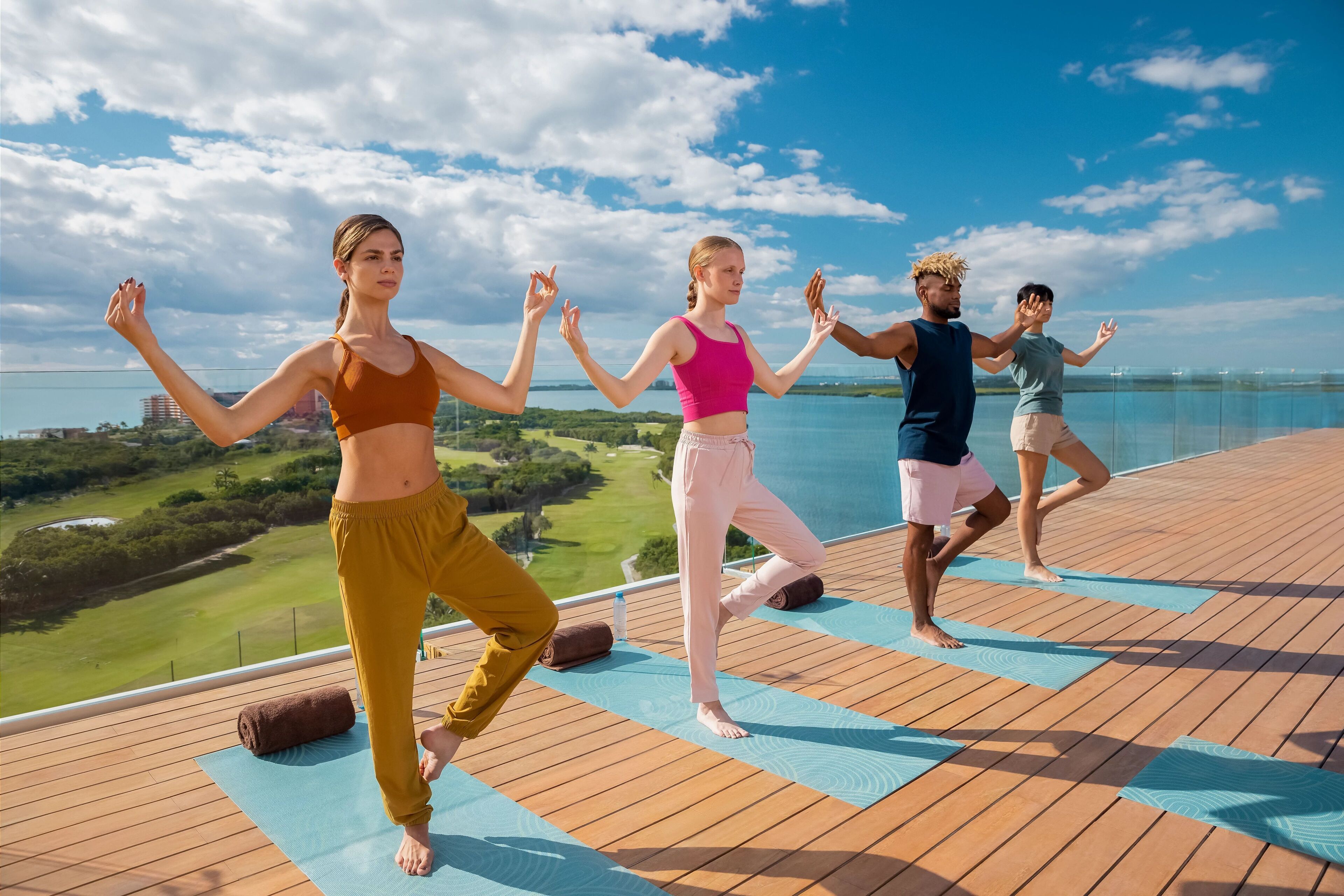 A group of people performing a yoga routine on a wooden deck with a scenic view of a golf course and water body.