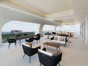 A modern outdoor lounge area with seating and tables, large windows offering city views, and a contemporary architectural design.