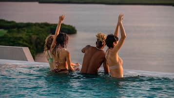 Un groupe de personnes se trouve dans une piscine, avec en arrière-plan une étendue d’eau et de la végétation.