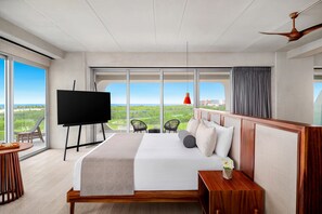 A modern hotel room with a large bed, a TV, a dining table, and a balcony with a view.