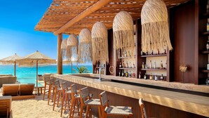 Un bar frente a la playa con sillas de madera y una barra, con vistas al océano.